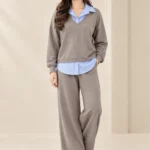 Woman wearing a taupe-grey V-neck sweatshirt and matching wide-leg trousers with a blue-and-white striped shirt