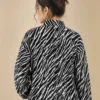 Woman wearing a black and white zebra print zip-up jacket with long sleeves and side pockets.