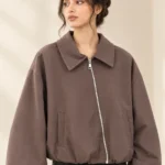 Woman wearing a taupe brown zip-up bomber jacket with a wide pointed collar, voluminous sleeves and front pockets.