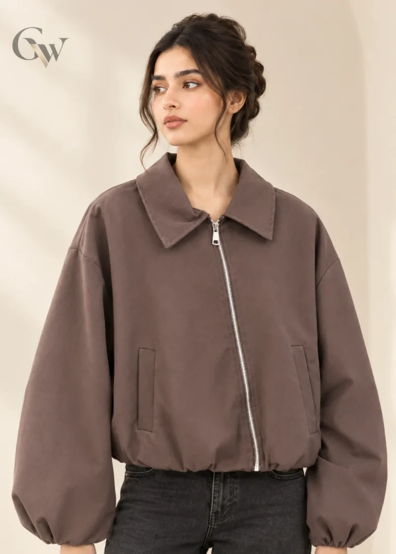 Woman wearing a taupe brown zip-up bomber jacket with a wide pointed collar, voluminous sleeves and front pockets.